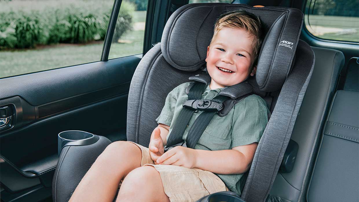 Smiling toddler sitting forward-facing in a Chicco OneFit LX ClearTex car seat inside a vehicle.